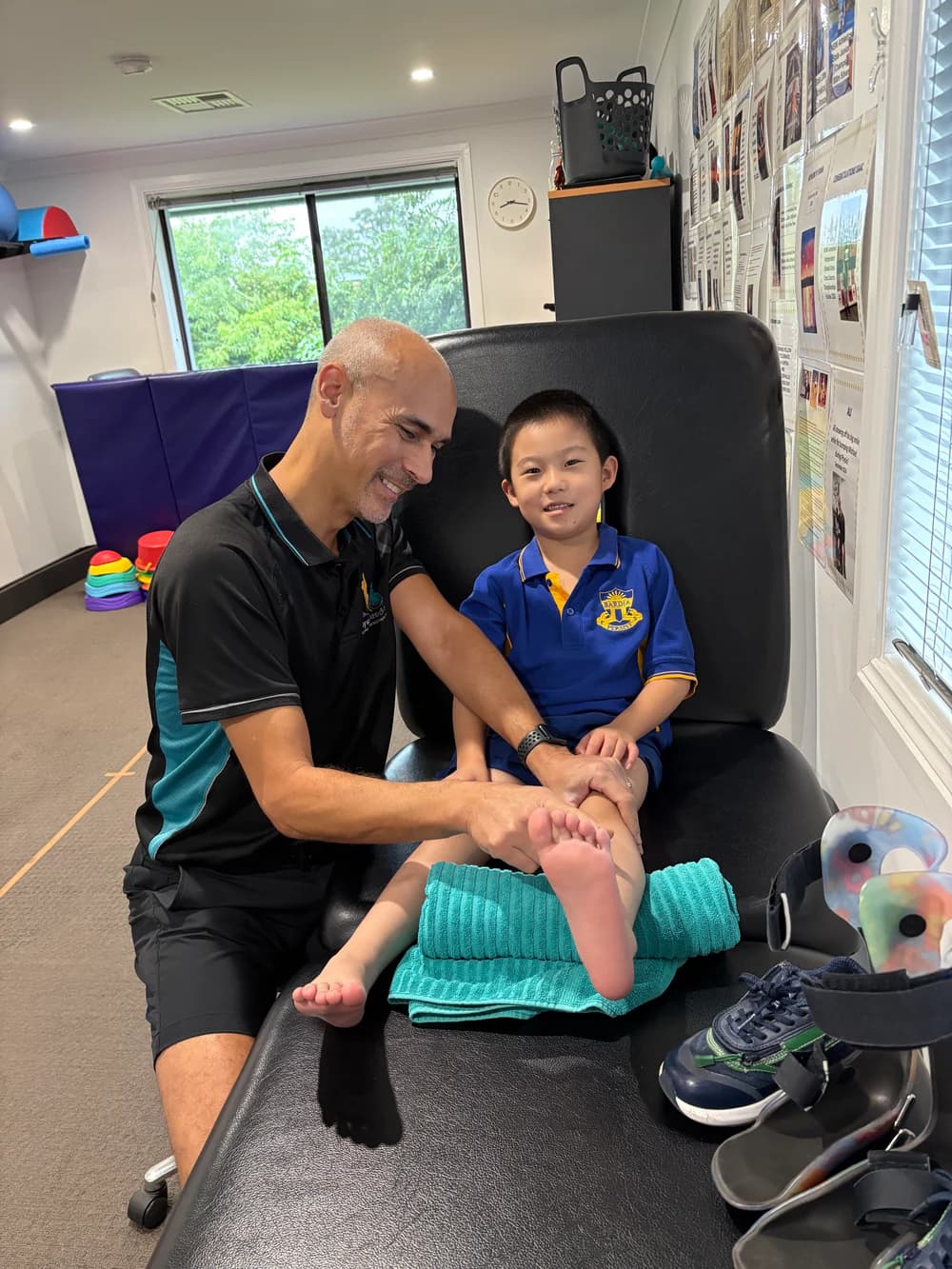 A physio working on a smiling boy's ankle on the plinth